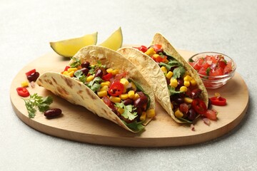 Tasty vegetarian tacos with beans, vegetables and lime on light grey table, closeup