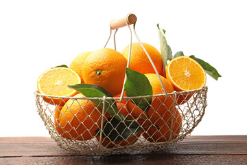 Juicy oranges and green leaves in metal basket on wooden table against white background