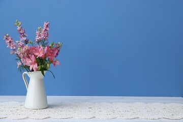 Beautiful flowers in vase on white wooden table against light blue background, space for text