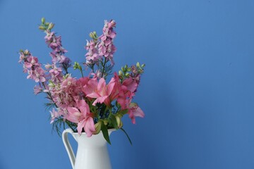 Beautiful flowers in vase on light blue background, closeup. Space for text