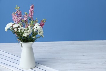 Beautiful flowers in vase on white wooden table against light blue background, space for text