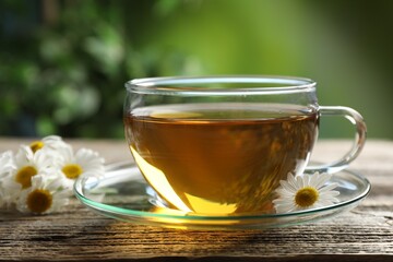 Aromatic tea in glass cup and chamomile flowers on wooden table, closeup