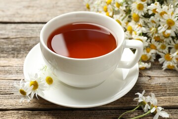 Aromatic tea in cup and chamomile flowers on wooden table, closeup