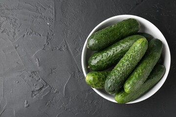 Fresh cucumbers in bowl on dark textured table, top view. Space for text