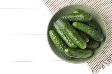 Fresh cucumbers in bowl on white wooden table, top view. Space for text