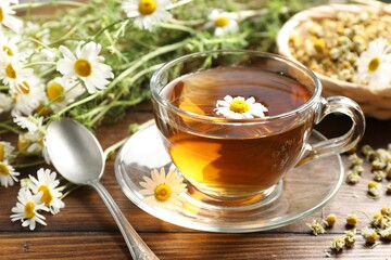 Tasty chamomile tea and flowers on wooden table, closeup