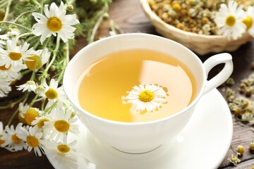 Tasty chamomile tea and flowers on wooden table, closeup