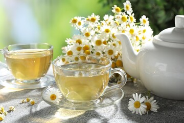 Tasty chamomile tea and flowers on light grey table, closeup