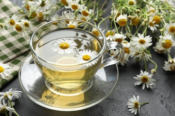 Tasty chamomile tea and flowers on black table, closeup