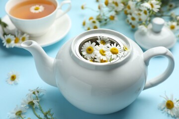 Teapot with chamomile flowers on light blue background, closeup