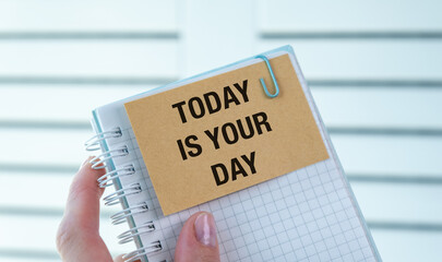 A person holding a notebook with a note that says Today is Your Day