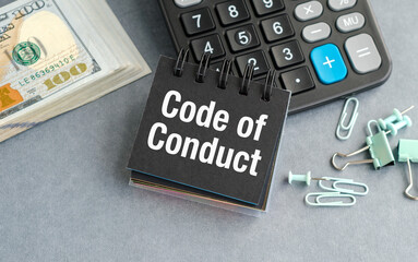 A calculator sits on a desk with a piece of paper that says Code of Conduct