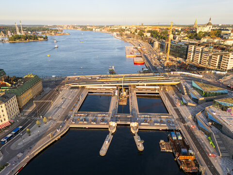 Aerial view of tranquil waters reflecting the sky, contrasting with the modern architecture and construction cranes along the waterfront near Slussen, Stockholm, Sweden.
