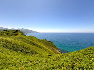 A breathtaking coastal landscape, where lush green hills meet the endless blue of the sea. The...