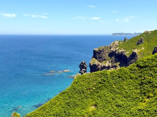 A stunning seaside cliff along coastline, where bright blue waters meet steep green slopes. This...