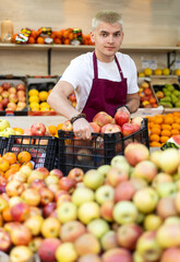 Shop seller puts goods on display case. Guy creates pyramid of apple, presents fresh goods....
