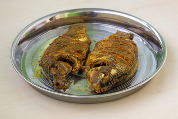 Crispy fried whole tilapia fish served on a steel platter. Authentic spicy BBQ fish, perfectly...
