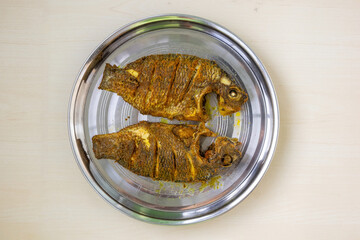 Crispy fried Tilapia fish, two whole servings on a sleek steel plate, set against a warm wooden...