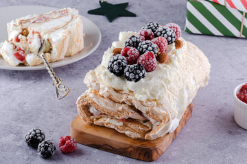 A rich meringue dessert presented on a wooden board, filled with cream and adorned with raspberries and blackberries. Perfect for holiday celebrations or special occasions.