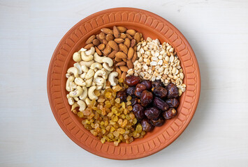 Healthy eating assortment featuring almonds, cashews, peanuts, dates, and raisins, beautifully presented on a natural clay plate. Ideal for wellness and nutritious snack visuals. Top view.