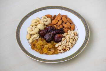 Assorted healthy nuts and dried fruits—almonds, cashews, peanuts, dates, raisins—artfully arranged on a clean white plate. Perfect for wellness and healthy lifestyle themes.