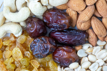Close-up texture of assorted dry fruits like dates, almonds, cashews, peanuts, and raisins, perfect for healthy diet backgrounds.