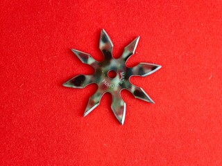 A star-shaped shuriken painted in military colors on a red background. The inscription on the shuriken reads Made in China.
