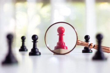 Magnifying glass searching red chess pawn standing out among black pawns. Concept of uniqueness,...