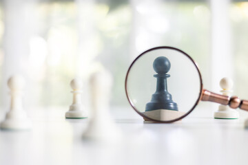 Magnifying glass searching black chess pawn standing out among white pawns. Concept of uniqueness,...