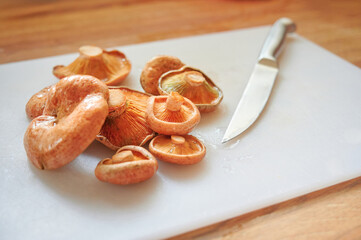 Spanish niscalos, saffron milk caps (Lactarius deliciosus) on cutting board with knife in kitchen. Traditional Spanish autumn recipes with seasonal edible mushrooms.