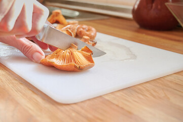 Unrecognizable woman cutting some saffron milk caps (Lactarius deliciosus) on the cutting board to cooke them in the kitchen. Preparing traditional autumn recipes with seasonal edible mushrooms.