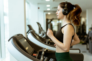 Running on a treadmill in a modern gym while listening to music on headphones