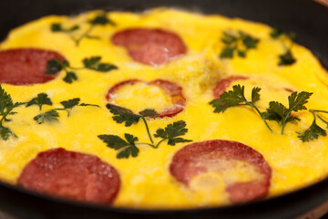 A close-up of a cooked omelette with slices of sausage and fresh cilantro on top