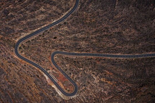 Aerial view of a winding road cuts a stark path through the rugged, arid landscape, revealing the island's volcanic origins, La Gomera, Canary Islands, Spain.