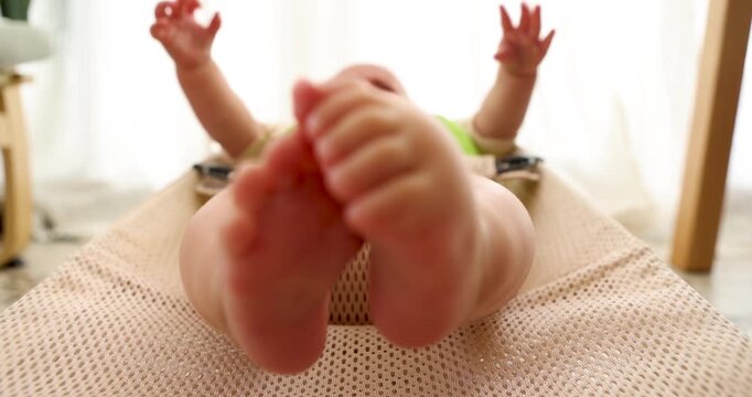 Cheerful infant lying comfortably on bouncer, vigorously kicking legs and waving arms, wearing soft bib and diaper, experiencing playful developmental moments with unrestrained joy