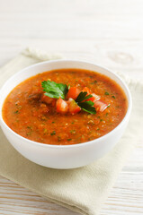 Cold summer soup Gazpacho in a white bowl on a napkin on the table. Traditional Spanish cuisine concept. Vegan or vegetarian. Selective focus. Vertical orientation.