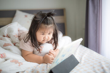 A little Asian girl is lying on the bed watching a tablet,Asian girl lying on bed in bedroom and...