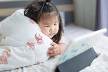 A little Asian girl is lying on the bed watching a tablet,Asian girl lying on bed in bedroom and...