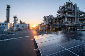 Fototapeta premium Industrial refinery with complex metal structures and solar panels under a clear sky at sunrise.