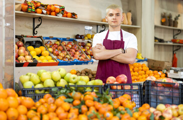 Guy seller stands in trading hall of vegetable store, wearied in apron stands in trading hall of minimarket, ready to greet visitors and offer food stuff. .
