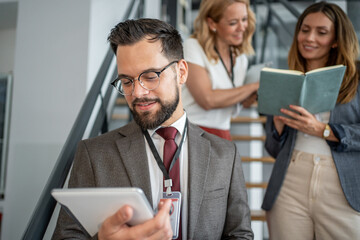 Businessman using digital tablet on stairs in office with colleagues discussing behind