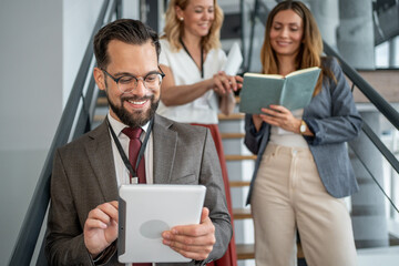 Smiling businessman using tablet on stairs with colleagues discussing in background