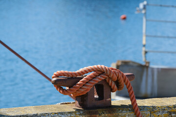 Pink rope or hemp securing a fishing trawler on a rusty bollard on a working dock and harbor in Nova Scotia