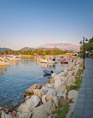 Morning light bathes the Moonlight beach in Kemer, Turkey. Boats rest in the calm bay with turquoise Mediterranean sea water. Lush green hills with palm trees seen at horizon