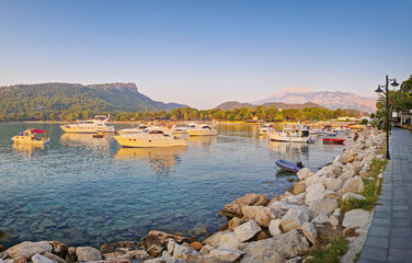 Morning light bathes the Moonlight beach in Kemer, Turkey. Boats rest in the calm bay with turquoise Mediterranean sea water. Majestic Taurus mountains with Olympos peak Tahtali in the background