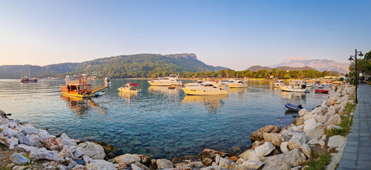Morning light bathes the Moonlight beach in Kemer, Turkey. Boats rest in the calm bay with turquoise Mediterranean sea water. Majestic Taurus mountains with Olympos peak Tahtali in the background