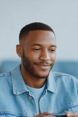 Obraz premium close-up of young black man smiling while playing handheld console blurred couch behind natural light