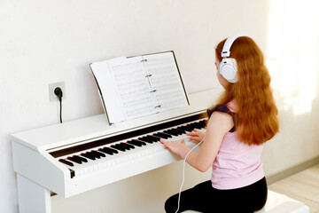 girl student with red hair in headphones learns to play the piano