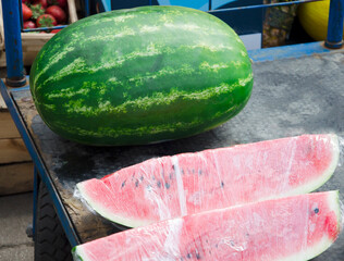 Close-up view of fresh ripe watermelon slices wrapped in plastic film and displayed on black and...