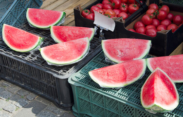 Close-up view of fresh ripe watermelon slices wrapped in plastic film and displayed on black and...